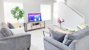 Un salon moderne avec un téléviseur à écran plat, des canapés gris, une table basse et un escalier.
