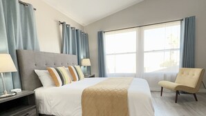 Une chambre d’hôtel moderne avec un grand lit, une table de chevet, une chaise et une fenêtre avec des rideaux.