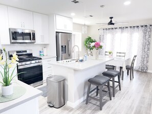 A modern kitchen with white cabinets, stainless steel appliances, a central island with bar stools, and a dining area with a table and chairs.