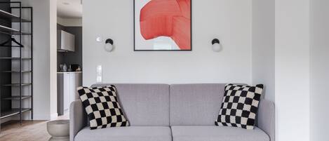 Una sala moderna con un sofá gris, almohadones de cuadros, un cuadro abstracto enmarcado y un diseño minimalista.