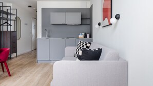 Een moderne, compacte leefruimte met een kitchenette, een grijze bank en een rode fauteuil.