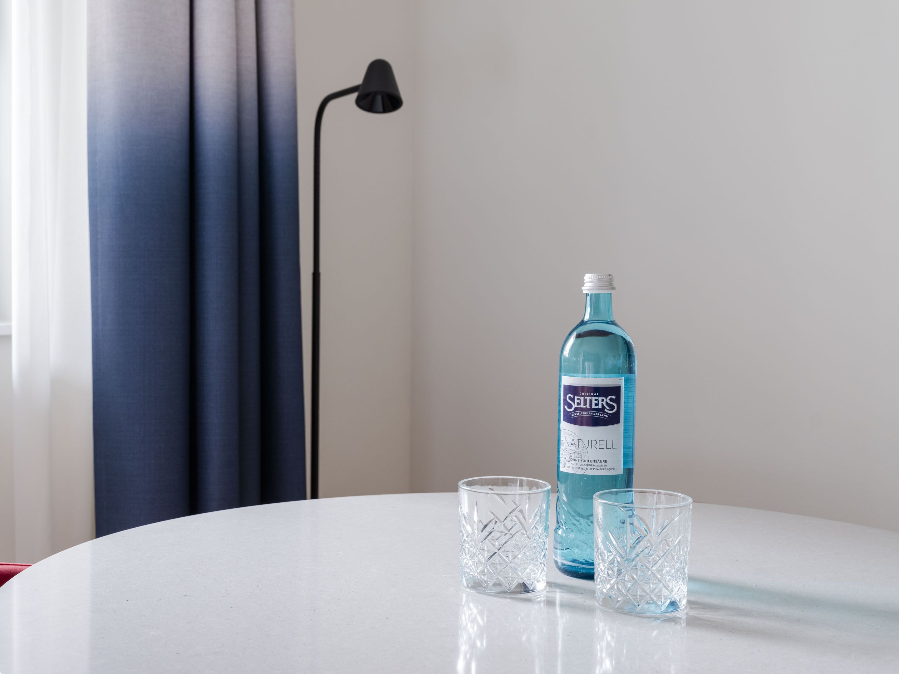 A bottle of Seiters Naturell water and two glasses on a white table.