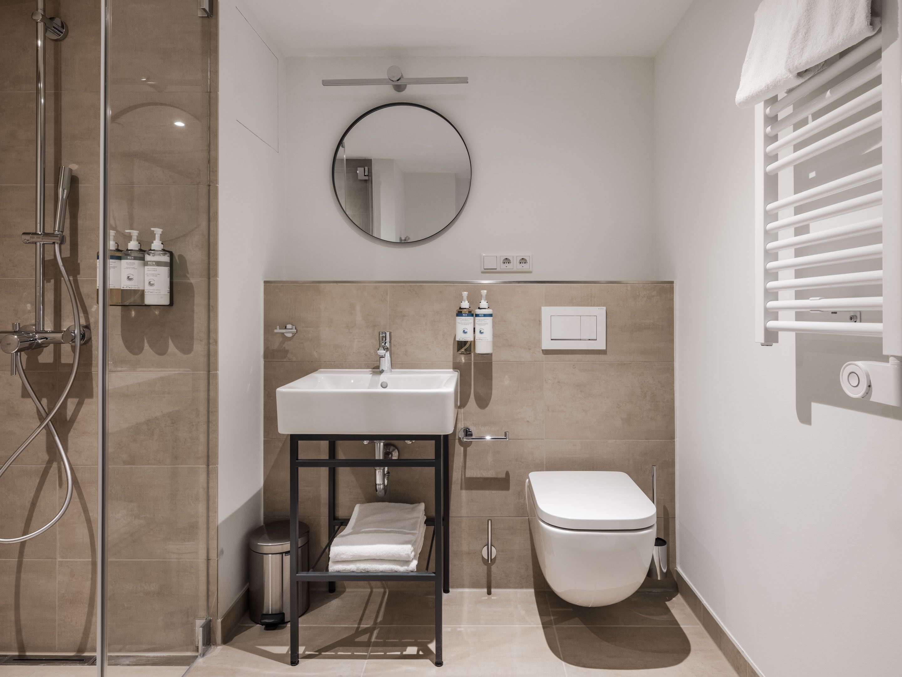 Een moderne badkamer met een douchecabine van glas, een witte wastafel met zwarte omlijsting, een toilet en een handdoekhouder.