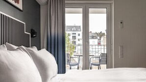 Een hotelkamer met een bed, een stadszicht vanaf een balkon en een stoel ernaast.
