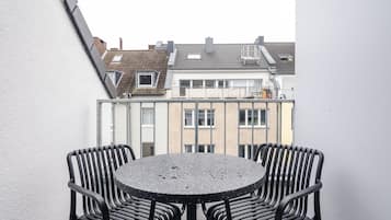 A balcony with two black metal chairs and a round table, overlooking a row of residential buildings.