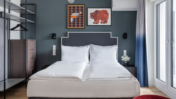 Een moderne slaapkamer met een bed, een kledingkast, een rode stoel en kunst aan de muur.