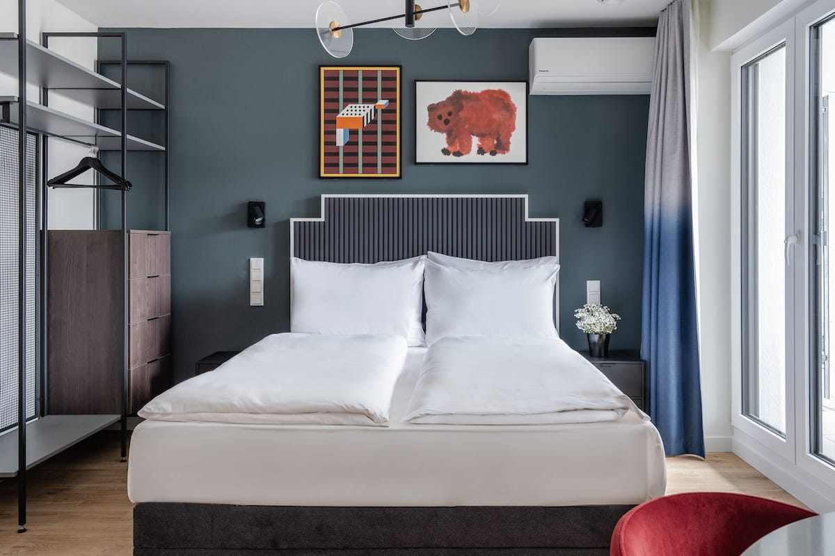 Quarto moderno com cama, guarda-roupa, uma cadeira vermelha e obras de arte na parede.