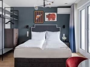 A modern bedroom with a bed, a wardrobe, a red chair, and artwork on the wall. - Numa Düsseldorf Leo (Düsseldorf)