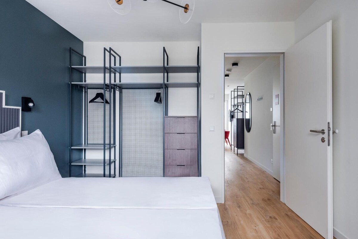 A modern bedroom with a bed, a wardrobe, and a built-in wardrobe with shelves.