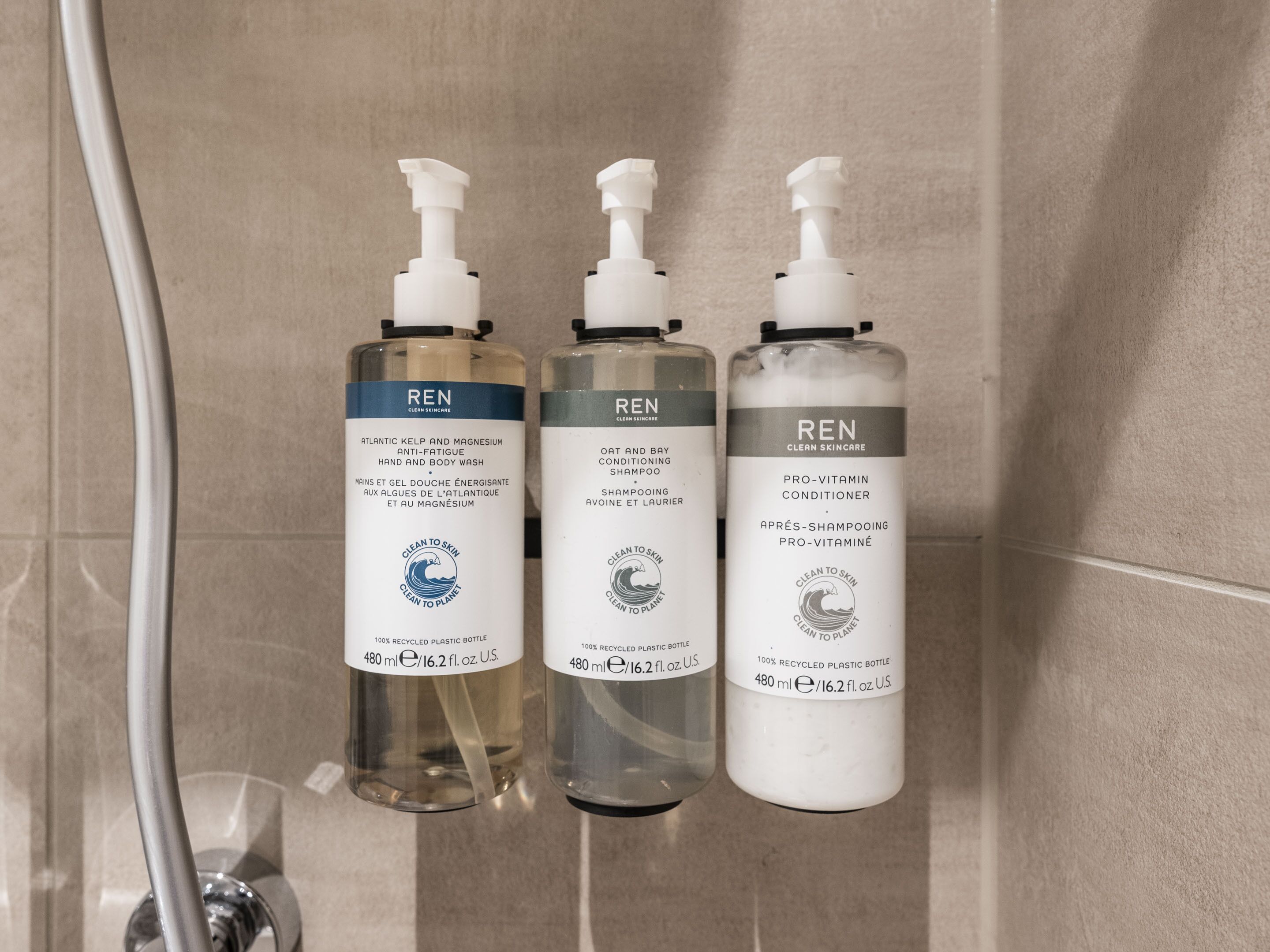 Trois flacons de produits de soins pour la peau de la marque REN sont posés sur le mur d’une salle de bain.