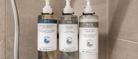 Trois flacons de produits de soins pour la peau de la marque REN sont posés sur le mur d’une salle de bain.