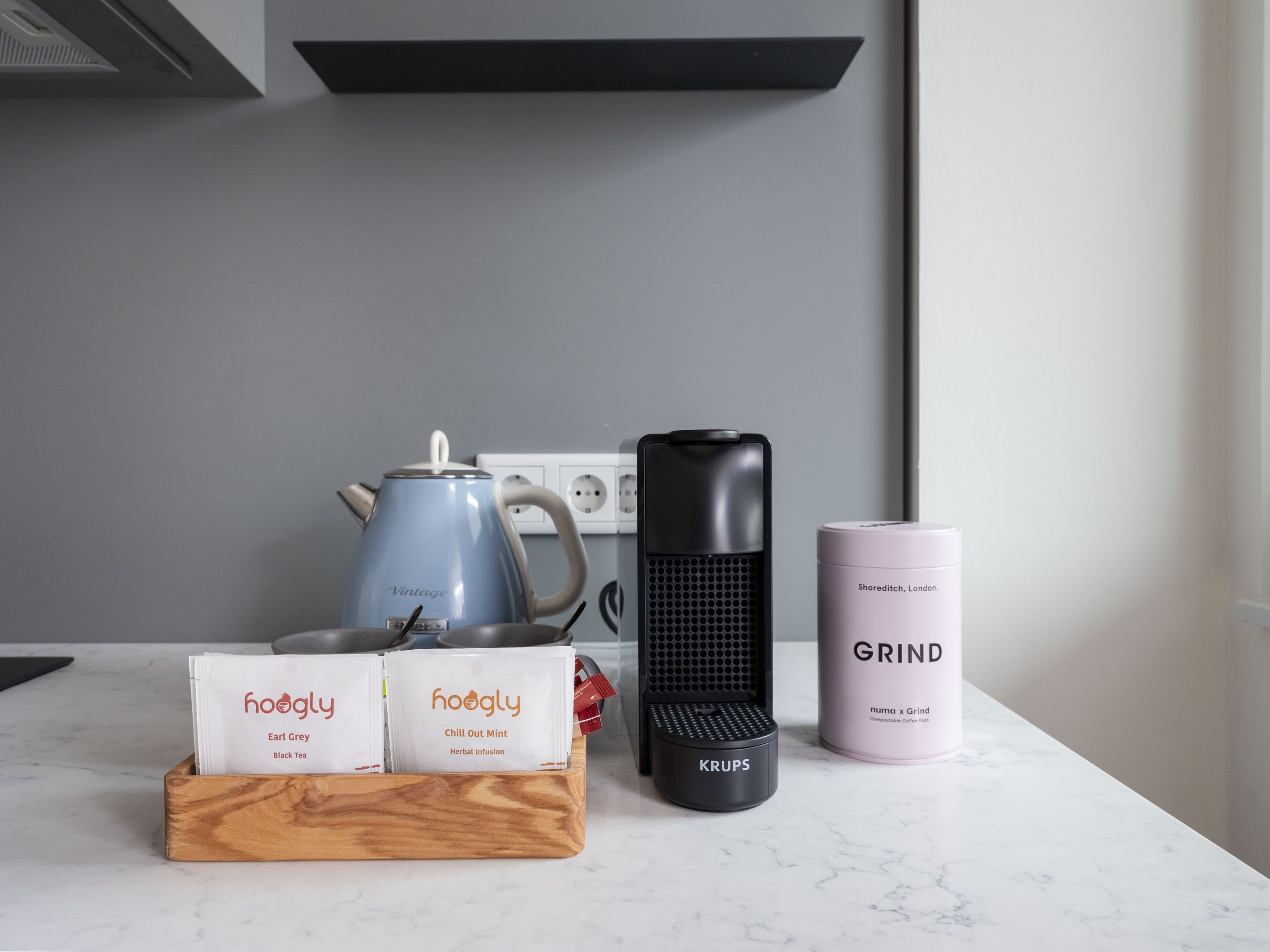 En køkkenbordplade med elkedel, kaffemaskine og en beholder med kaffekapsler.