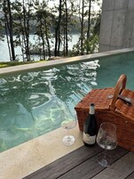 Escena junto a la piscina con una cesta de mimbre que contiene una botella y vasos, además de una terraza de madera.
