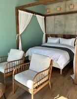 Una habitación con una cama, dos sillas de mimbre y una cama con dosel y cortinas blancas.