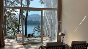 A bedroom with a large window, a ceiling fan, and a view of a lake and trees. - W181Ocean Stay (Geoje)