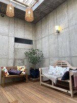 Una habitación acogedora con pared de concreto, un banco de madera, una cama de madera, una planta en maceta y dos lámparas de mimbre colgantes.