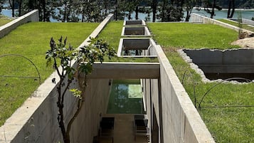 Ein modernes architektonisches Gebäude mit einem zentralen Wasserspiel, umgeben von gepflegtem Rasen und Bäumen.