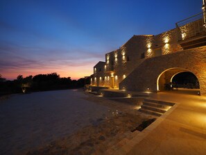 A stone building with a staircase leading to an upper level, a covered outdoor seating area, and a pool. - terra di pietra (East Mani)