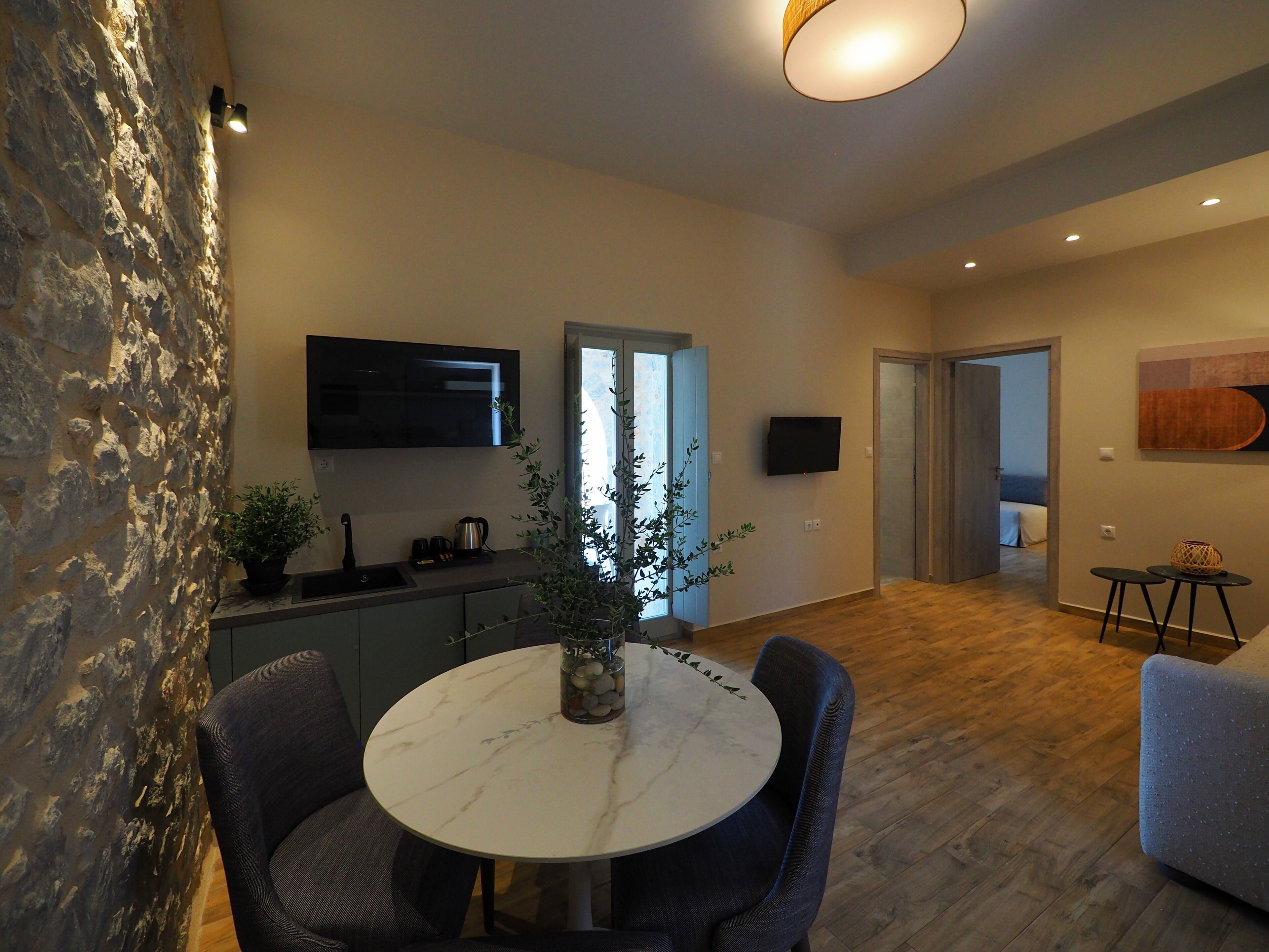 A modern kitchen with a built-in oven, a dining area with a marble table, and a living space with a TV and artwork.