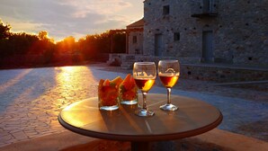 A table with three glasses of wine and a fruit bowl on a stone-paved patio with a stone building in the background. - terra di pietra (East Mani)