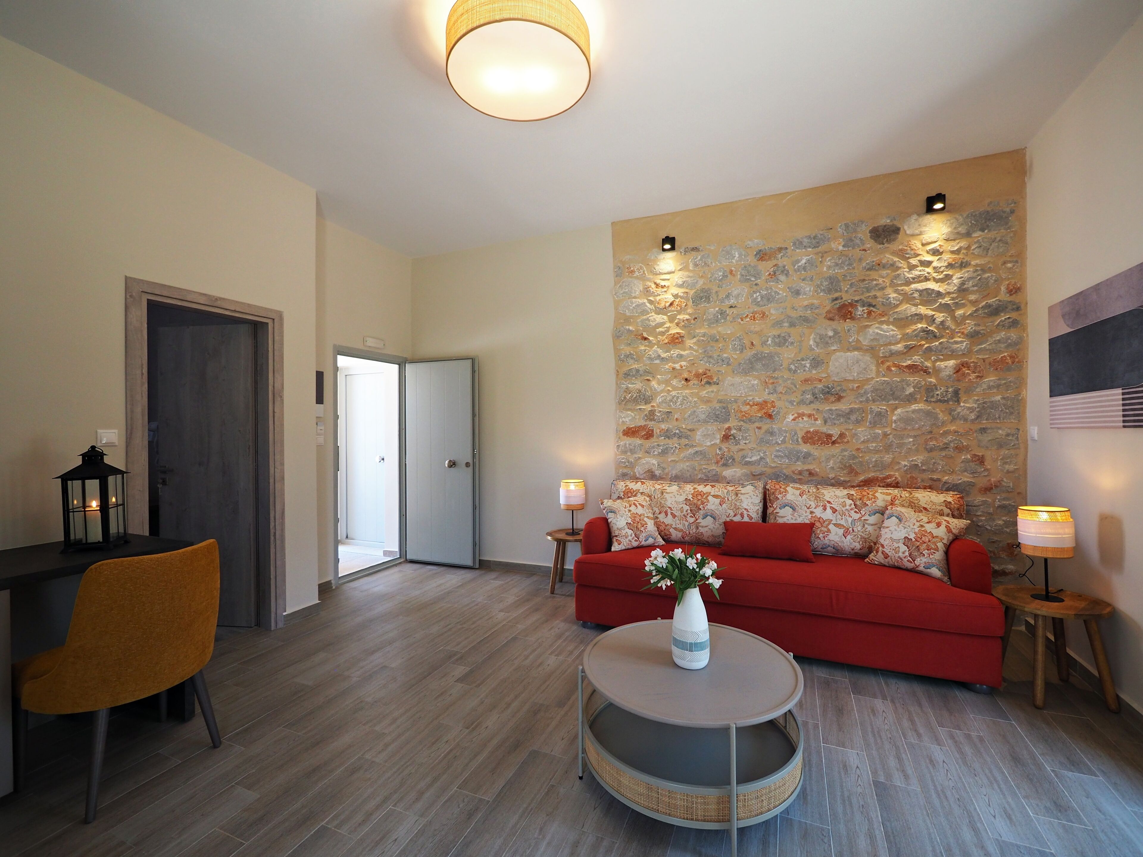 Een moderne woonkamer met een rode bank, een ronde salontafel en een stenen muur.