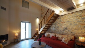 A spacious living room with a red sofa, a round coffee table, a wooden staircase, and a stone wall. - terra di pietra (East Mani)