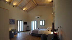 A spacious bedroom with a large bed, a desk with a candle, and a TV on the wall. - terra di pietra (East Mani)