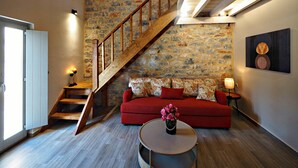 A cozy living room with a red sofa, a wooden staircase, and a stone wall. - terra di pietra (East Mani)
