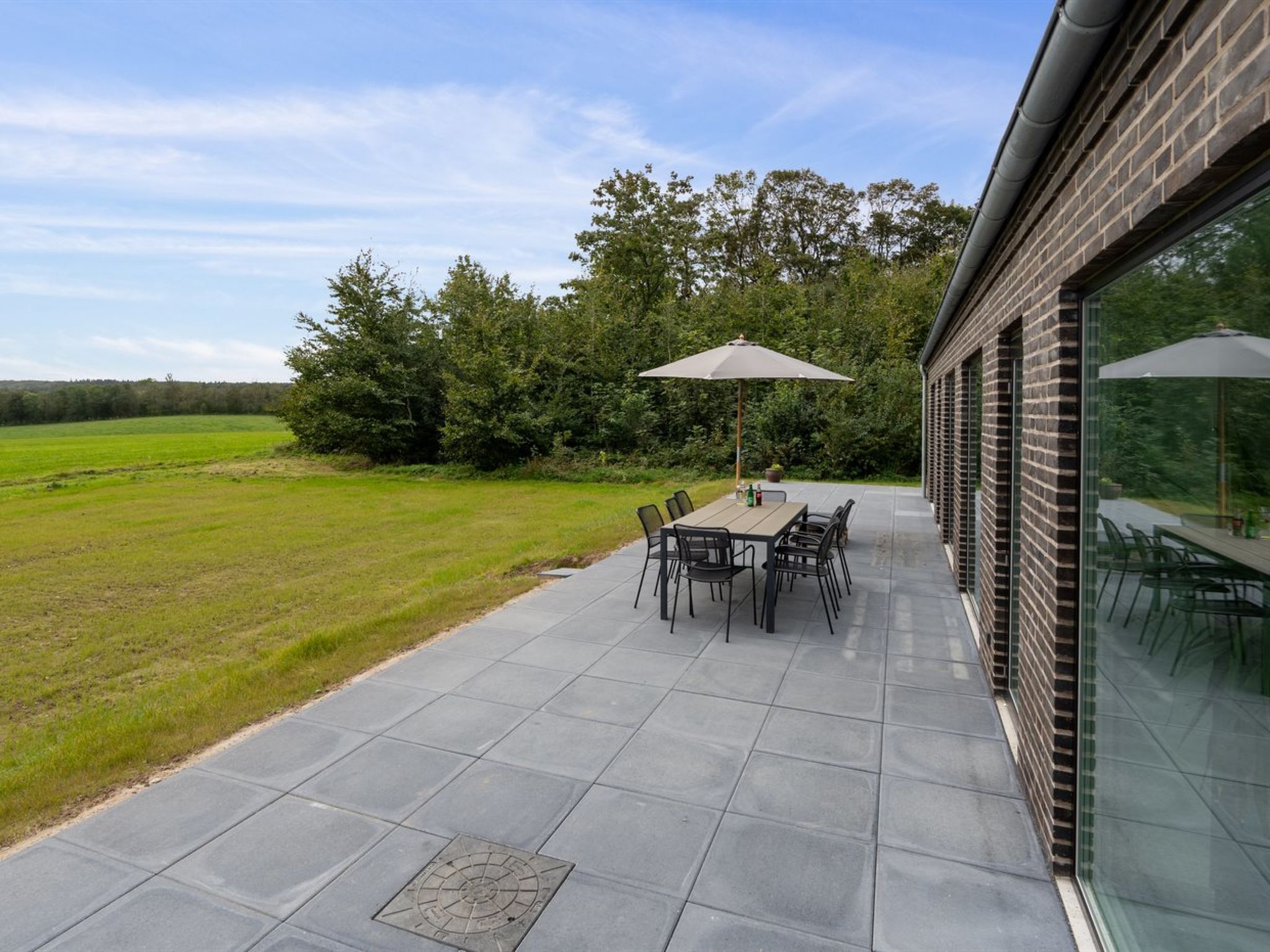 Eine Terrasse mit Tisch und Stühlen, ein Gulideckel und Blick auf ein Wiesenfeld mit Bäumen.