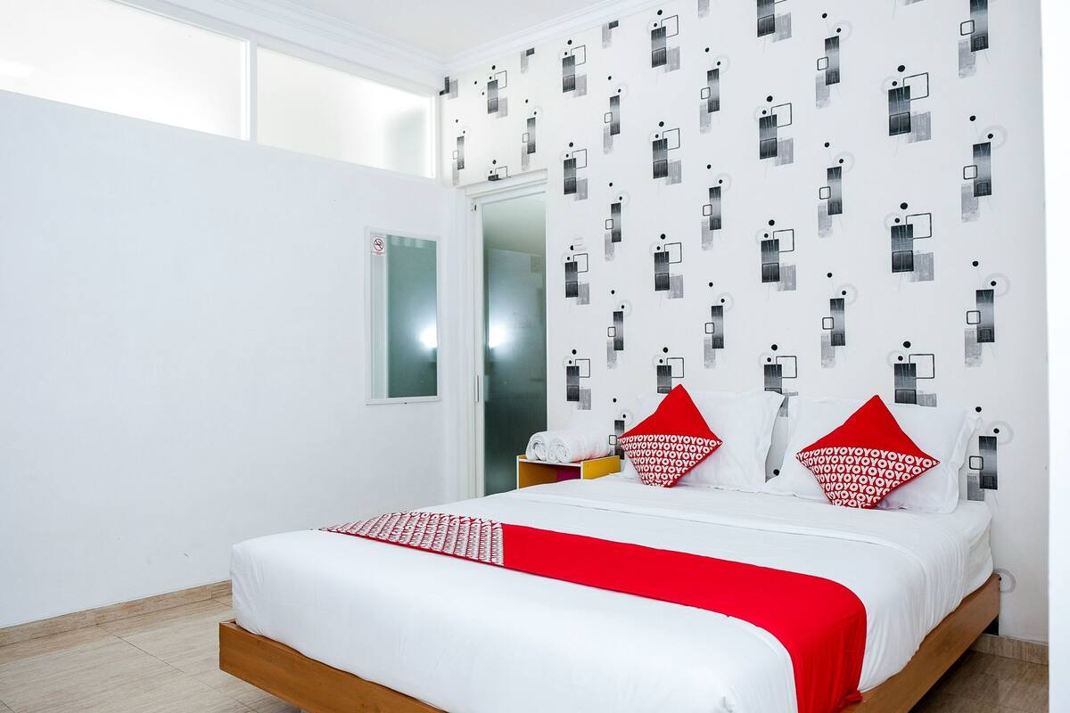 A modern hotel room with a large bed, white walls, and a patterned wallpaper.