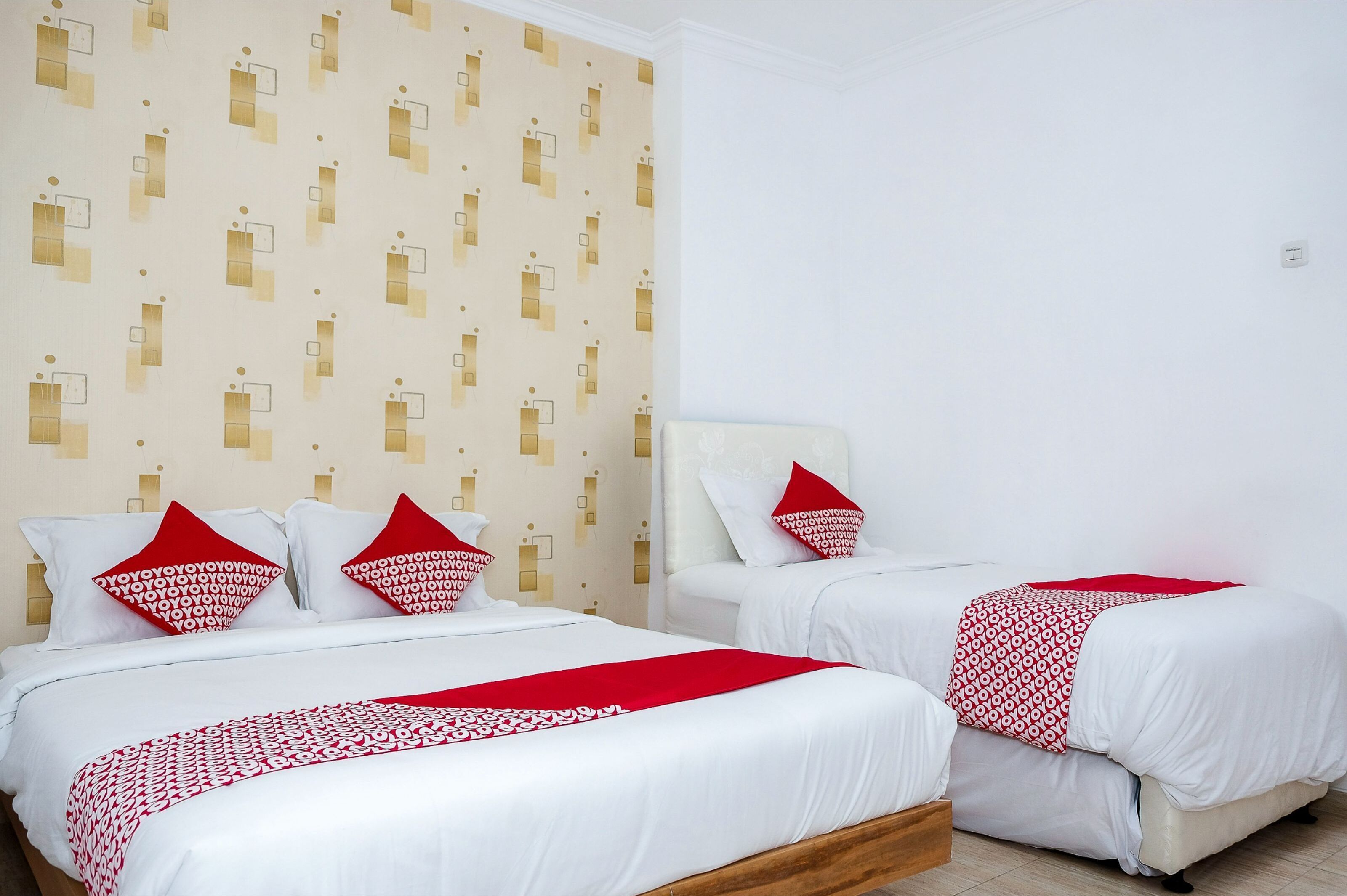 Una habitación de hotel con dos camas, ropa de cama blanca, almohadas rojas y un papel tapiz estampado.