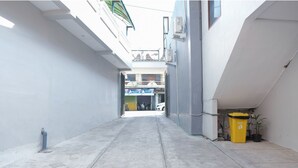 A narrow alleyway with a concrete floor, a yellow trash bin, and a potted plant. - Hotel O 111 Residence (Batu)