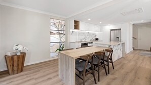 Une cuisine moderne avec des meubles blancs, un plan de travail en marbre et une table à manger en bois, accompagnée de chaises.
