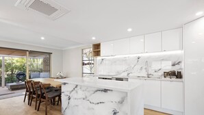 Une cuisine moderne dotée d’un îlot en marbre, de meubles blancs et d’un coin repas avec des meubles en bois.