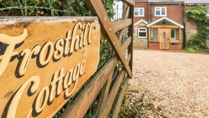Ein Holzschild mit der Aufschrift 'Frosthill Cottage', das ein Wohnhaus kennzeichnet.