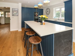 Una cocina con una isla grande, armarios azules, taburetes de madera e iluminación colgante.