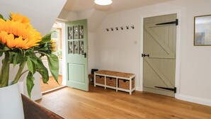 Ein Korridor mit Holzdielen, einer grünen Tür mit Glasfeldern, einer Bank mit Körben und einem an der Wand befestigten Kleiderhaken.