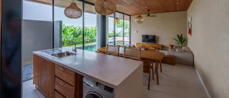 Una cocina moderna con lavadora incorporada, techo de madera y amplios ventanales con vista a zonas verdes.