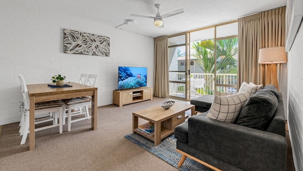 Una sala moderna con un sofá, una mesa de centro, un televisor y un comedor con una mesa y sillas.
