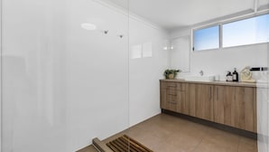 Un baño moderno con cabina de ducha de vidrio, tocador de madera con lavabo y ventana que proporciona luz natural.