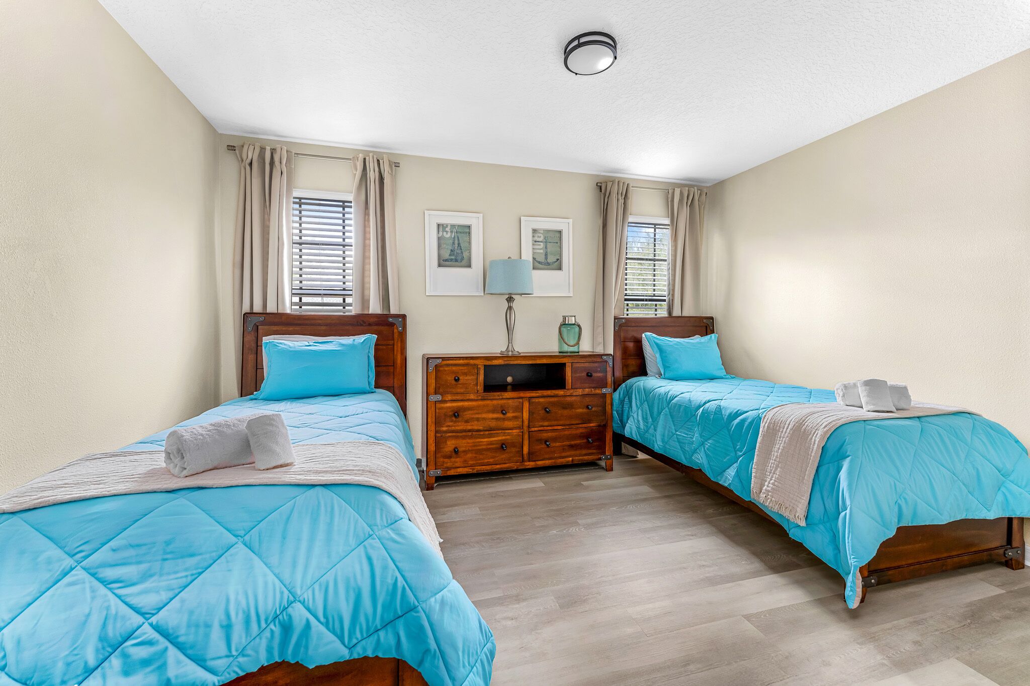A bedroom with two beds, a wooden dresser, and a ceiling light.