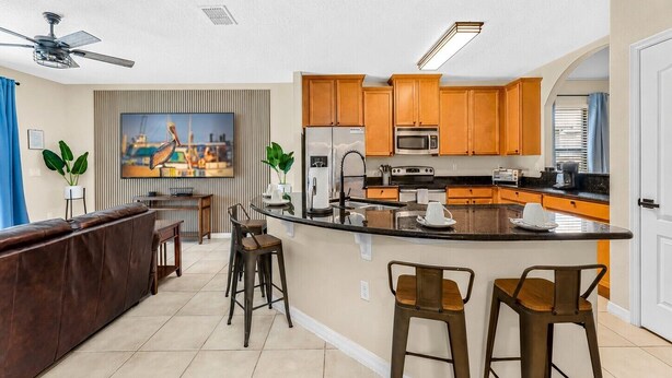 A modern kitchen with a central island, bar stools, and a ceiling fan.