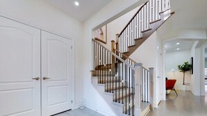 A staircase with a wooden handrail and black balusters, leading to a landing with a red chair and a potted plant. - GLOBALSTAY 4-Bd House Near Lake Simcoe (Georgina)