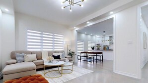 A modern living room with a sofa, coffee table, and orange ottoman. There is a kitchen area in the background with a dining table and chairs. - GLOBALSTAY 4-Bd House Near Lake Simcoe (Georgina)