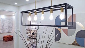 A modern interior with a geometric wall art, a suspended light fixture with five bulbs, and a seating area with a sofa and ottoman. - GLOBALSTAY 4-Bd House Near Lake Simcoe (Georgina)
