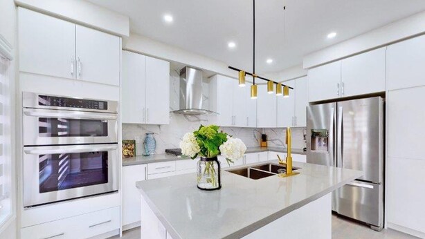 A modern kitchen with white cabinetry, stainless steel appliances, and a central island with a vase of flowers. - GLOBALSTAY 4-Bd House Near Lake Simcoe (Georgina)
