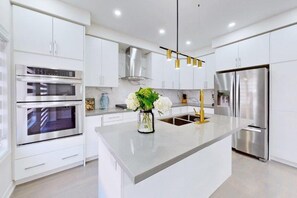 A modern kitchen with white cabinetry, stainless steel appliances, and a central island with a vase of flowers. - GLOBALSTAY 4-Bd House Near Lake Simcoe (Georgina)