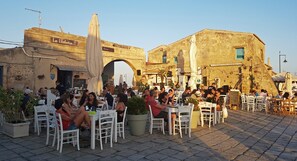 An outdoor café with white tables and chairs, a stone archway, and a building with a sign reading 'Le Balata.'