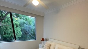 Un dormitorio con una cama grande, una mesita de noche, una lámpara y una ventana con vistas al verdor.