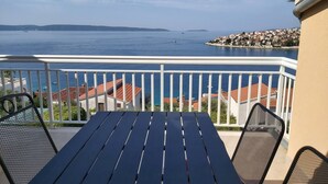A balcony with a table and chairs, overlooking a body of water and a coastal town. - Heated Infinity Pool, Family Apartment With Panoramic sea View 3 (Okrug)